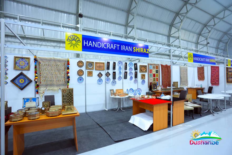 Exhibitor stands hung with embroidered textiles and painted ceramics under a Handicraft Iran Shiraz banner