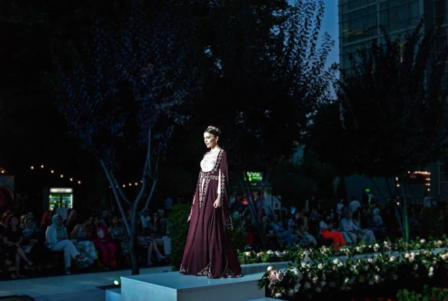 A model in a deep burgundy gown and jewelled headpiece walking the evening runway